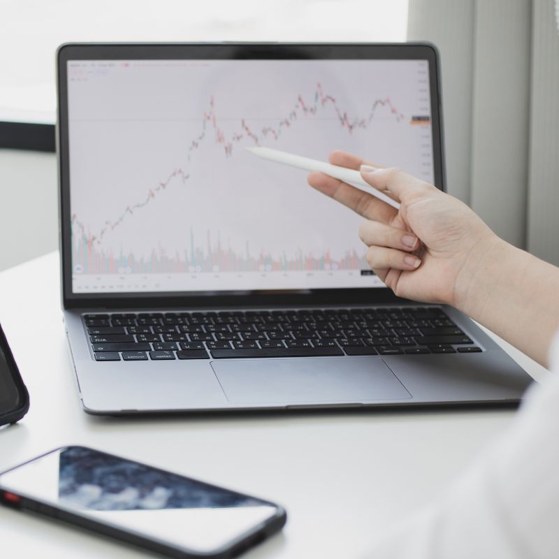 Main pointant un graphique boursier affiché sur un ordinateur portable lors d’une analyse des marchés financiers