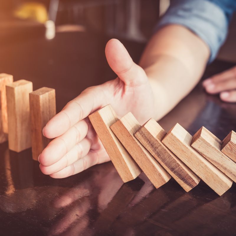 Prévention des risques financiers avec une stratégie de gestion de patrimoine, main arrêtant une chute de dominos